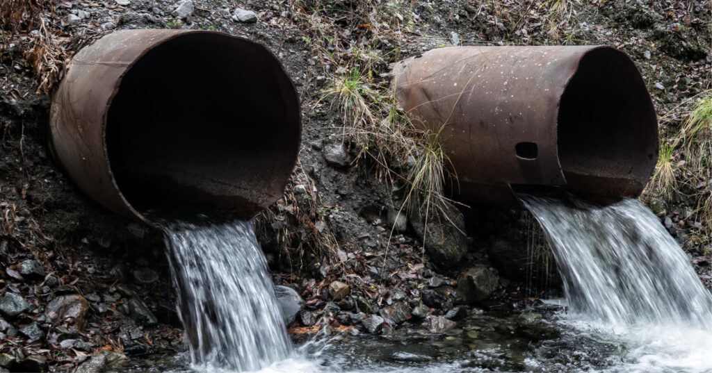 Deux tuyaux d'évacuation déversant de l'eau dans une rivière, symbolisant le transfert potentiel de métaux lourds et autres polluants dans les écosystèmes aquatiques